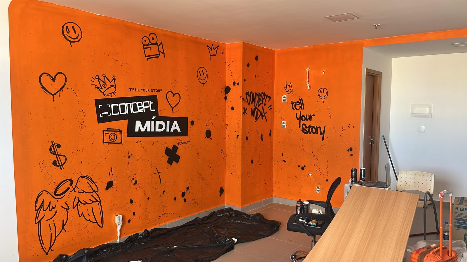 Parede do escritório da Concept Mídia pintada de laranja, com rabiscos em spray e a frase tell your story